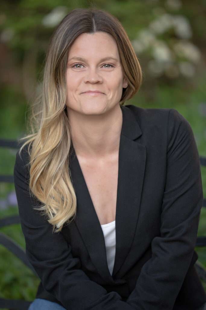 Smiling woman outdoors, professional headshot with greenery.