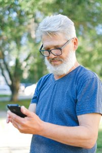 Senior man with glasses using smartphone outdoors.