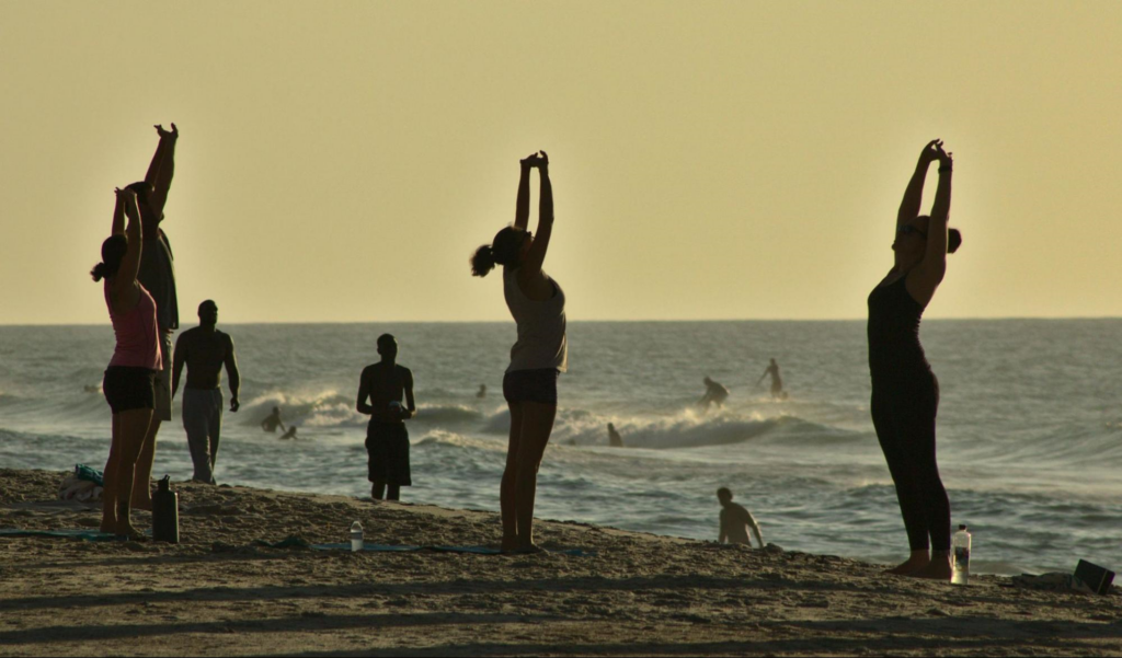 People practicing yoga on beach at sunset.
