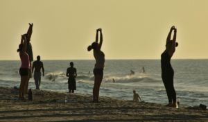 People practicing yoga on beach at sunset.