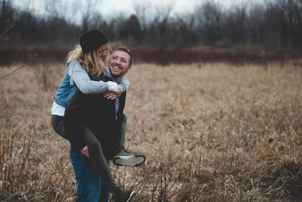 Happy couple enjoying piggyback ride in field.