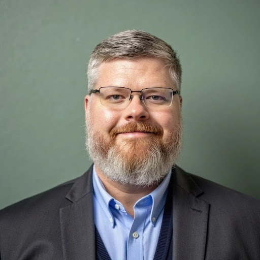 Man in suit with glasses smiling.