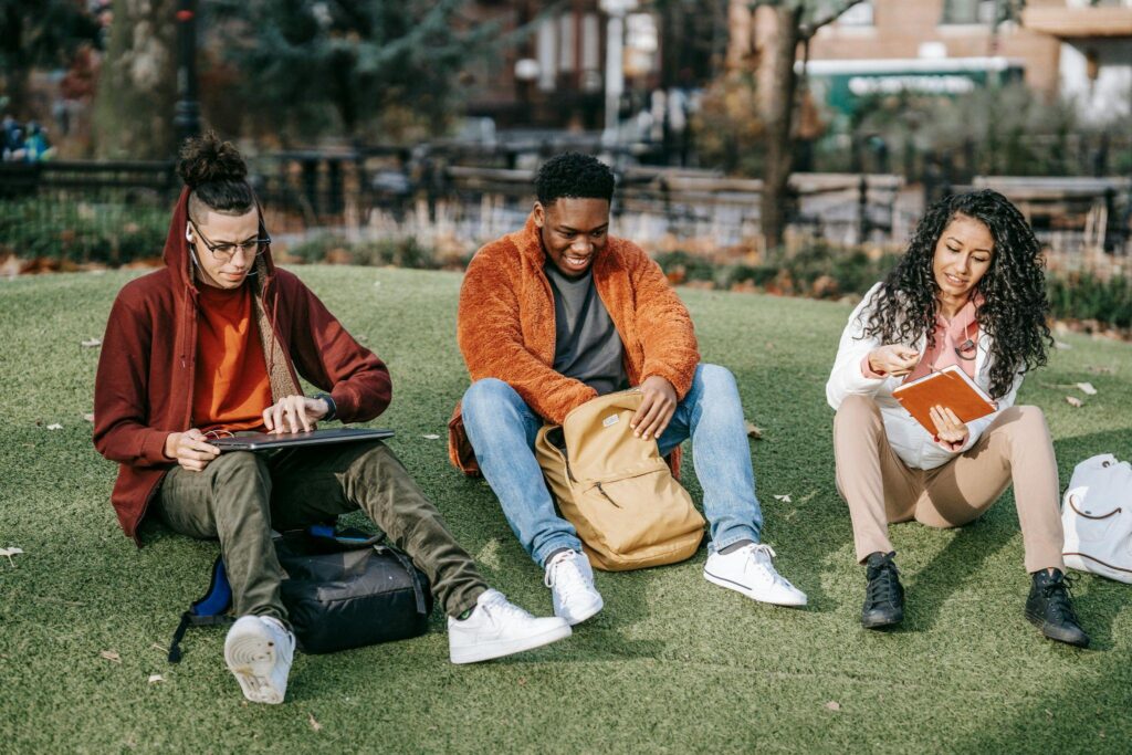 Three friends sitting on grass outdoors.