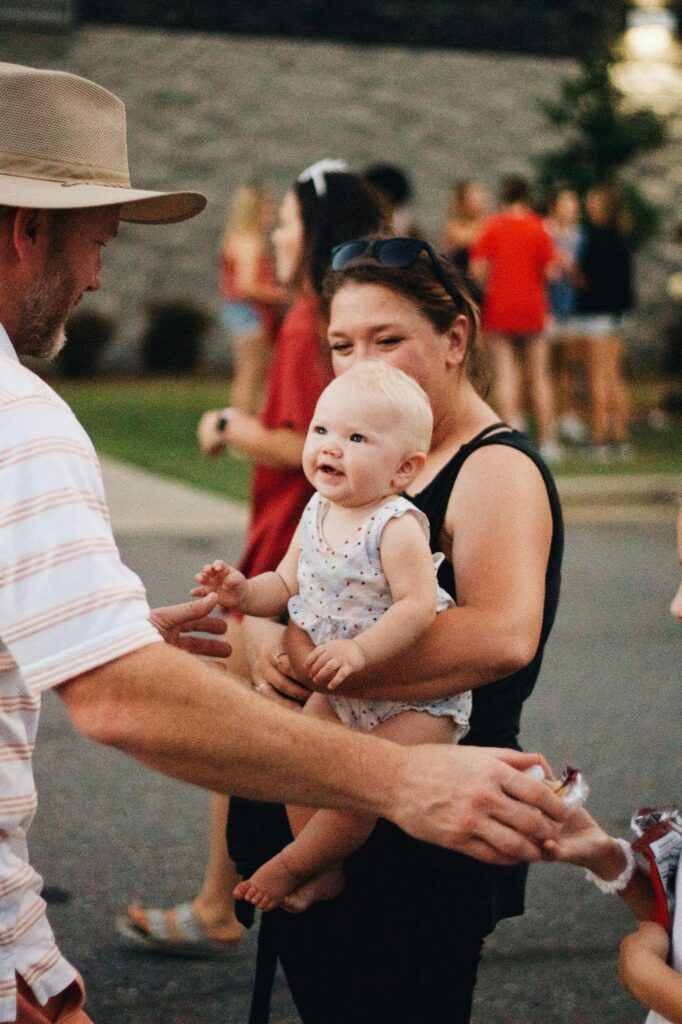 Baby smiles while held by parent outdoors.